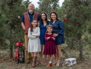 Group portrait in a pine forest setting with coordinated casual outfits and holiday decorations.