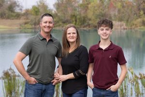 Family poses together for outdoor portrait photos near a scenic lake on a sunny autumn day.