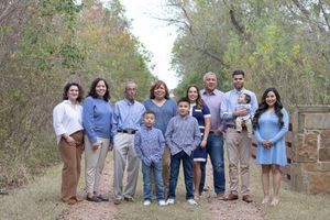 A group of people wearing coordinated blue and neutral tones pose together on a nature trail during autumn.