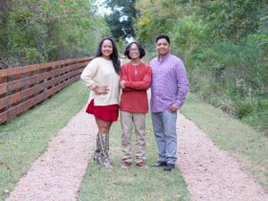 Three people standing together on dirt path wearing coordinated fall colors.