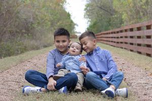 A family wearing coordinating denim and white outfits sits together on a wooden bridge for outdoor photos.