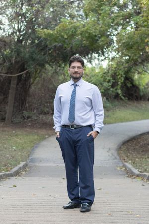 Professional wearing a light blue dress shirt and patterned tie walks along a curved concrete path outdoors.