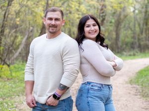 Couple in casual sweaters poses together on nature trail.