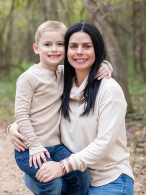 Mother and young child in matching cream sweaters share tender moment outdoors.