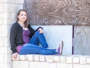 Casual portrait of person in black cardigan and jeans sitting on stone ledge.
