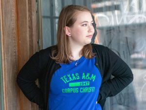 Student wearing Texas A&M Corpus Christi shirt poses against rustic door.