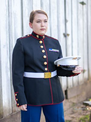 Marine in dress blues uniform holds white cover cap in formal portrait.