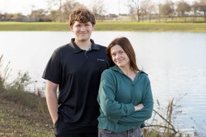 A couple poses together outdoors near a lake on a sunny day.