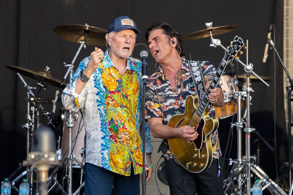 Two male performers singing together on stage at an outdoor concert.