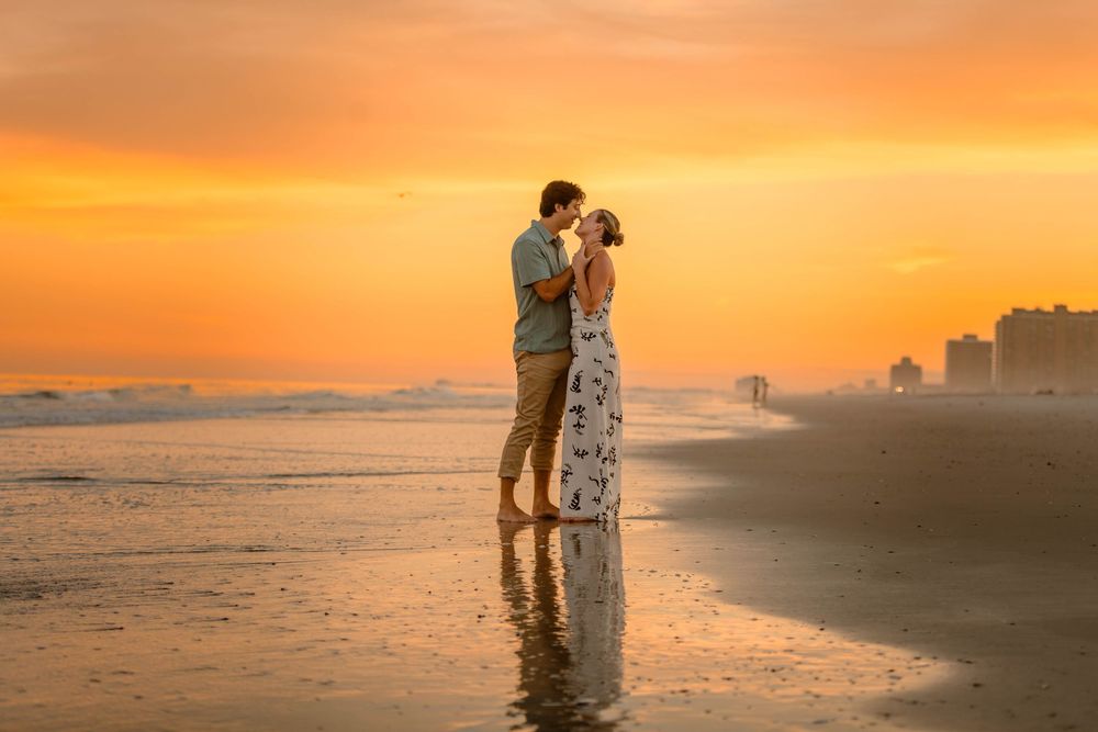 Couple sharing a romantic kiss on the beach during a stunning golden sunset with ocean waves reflecting the sky.