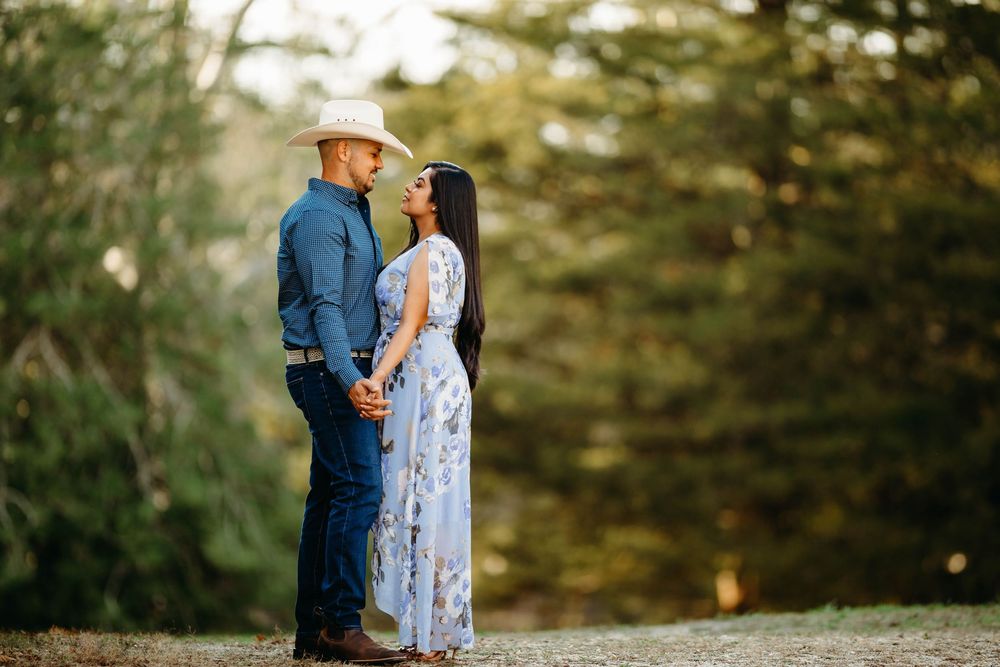 Couple holding hands in floral and denim outfits with cowboy hat in forest.