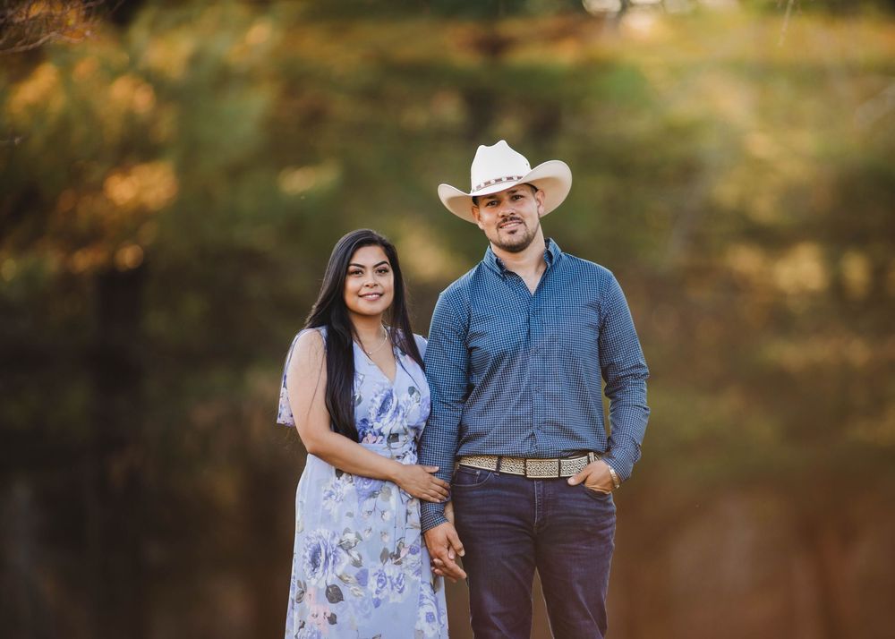 Smiling couple holding hands in blue outfits with cowboy hat in nature.