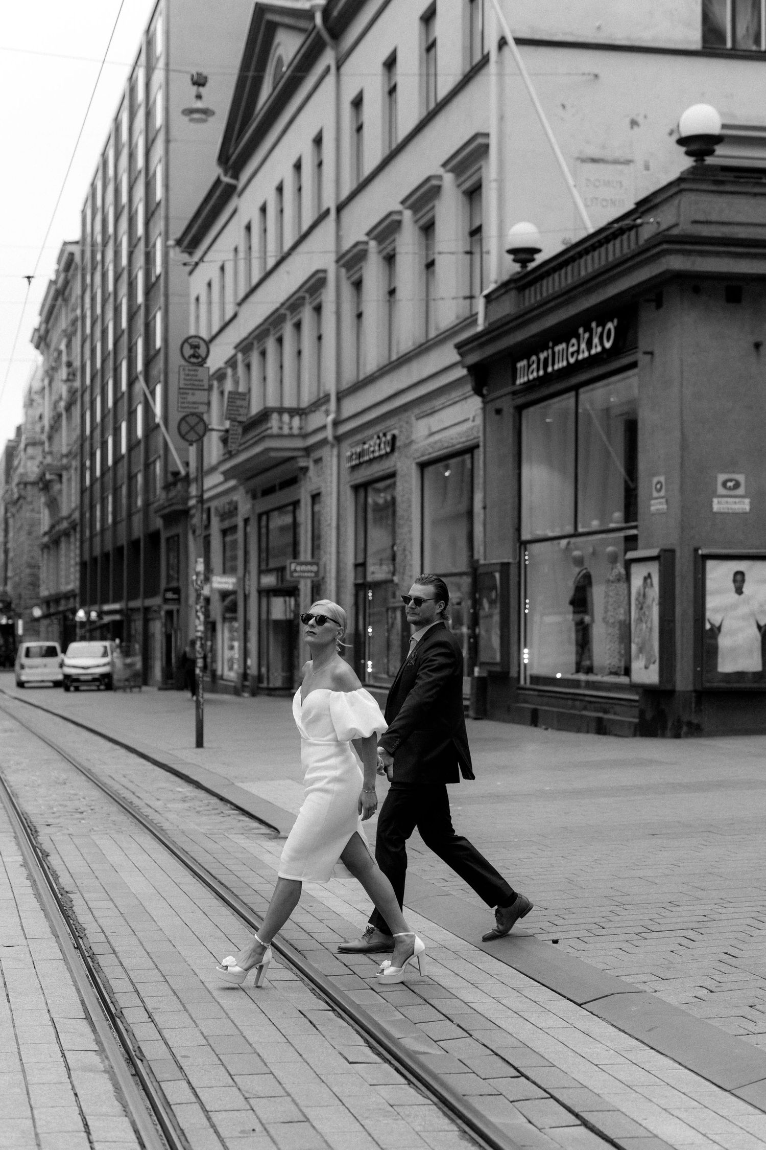 Urbaani hääpotretti jossa valkoasuinen nainen ja tummaan pukuun pukeutunut mies kävelevät käsi kädessä suojatien yli Helsingin keskustassa.