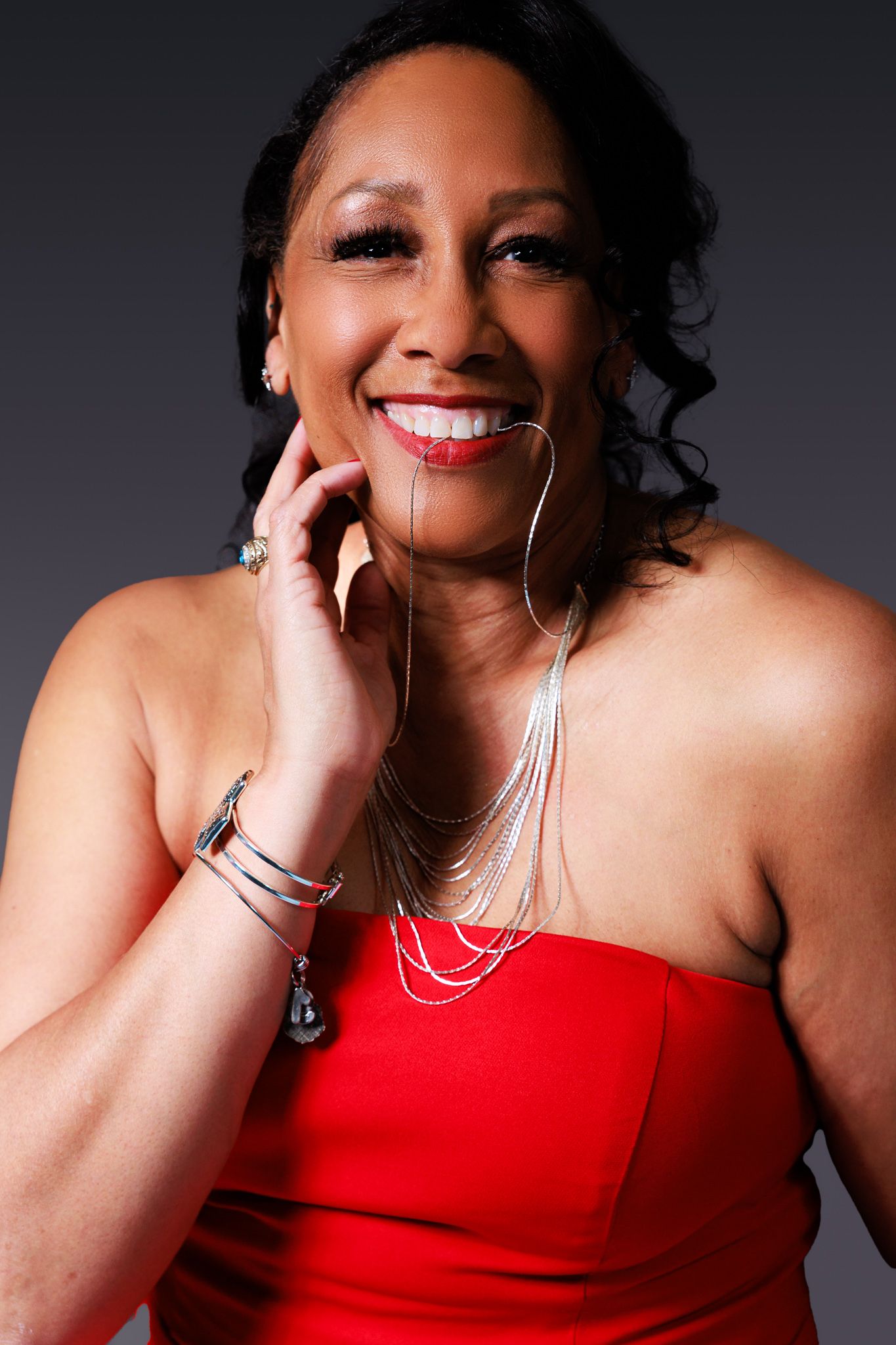 A series of portraits showing a woman in a red strapless dress against a dark background, smiling warmly.