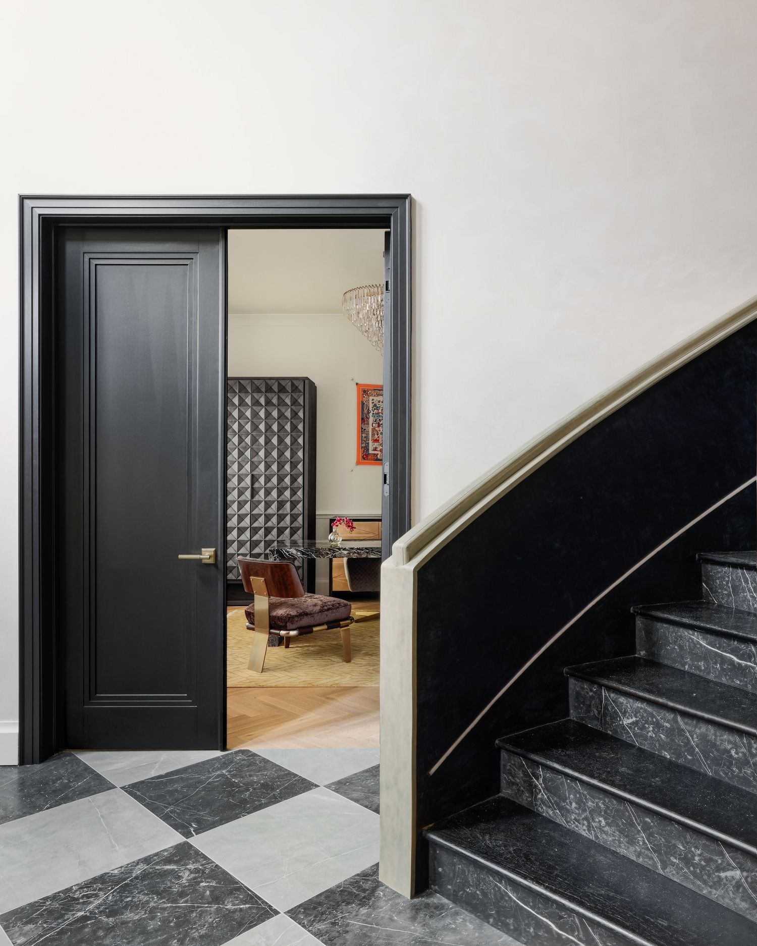 Elegant entryway with black paneled door, checkered marble floor, dark marble staircase, and cream handrail.