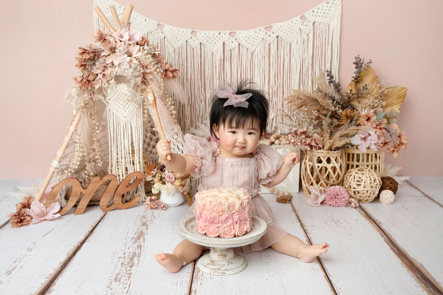Boho birthday setup with macrame backdrop, floral decorations and pink cake.