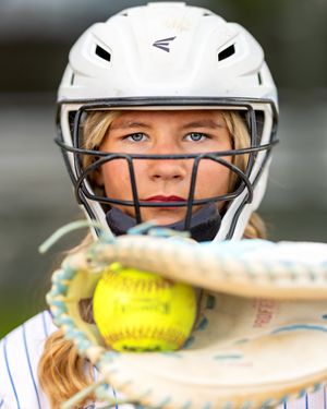Young softball player in Easton helmet holds yellow ball in glove, focused game-ready expression.