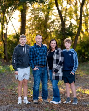 Family of four smiling outdoors in fall foliage, parents and two teenage boys in casual attire.
