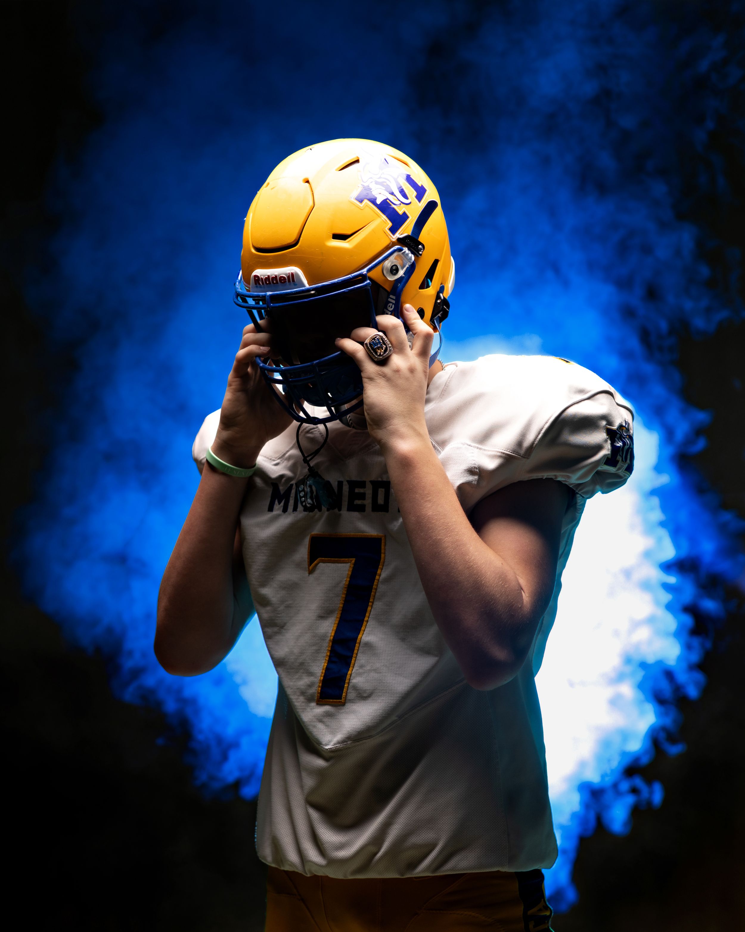 Football player in yellow helmet and number 7 jersey poses dramatically against blue smoke background.