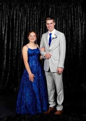 Young couple dressed in formal prom attire pose together in front of black sequin backdrop.
