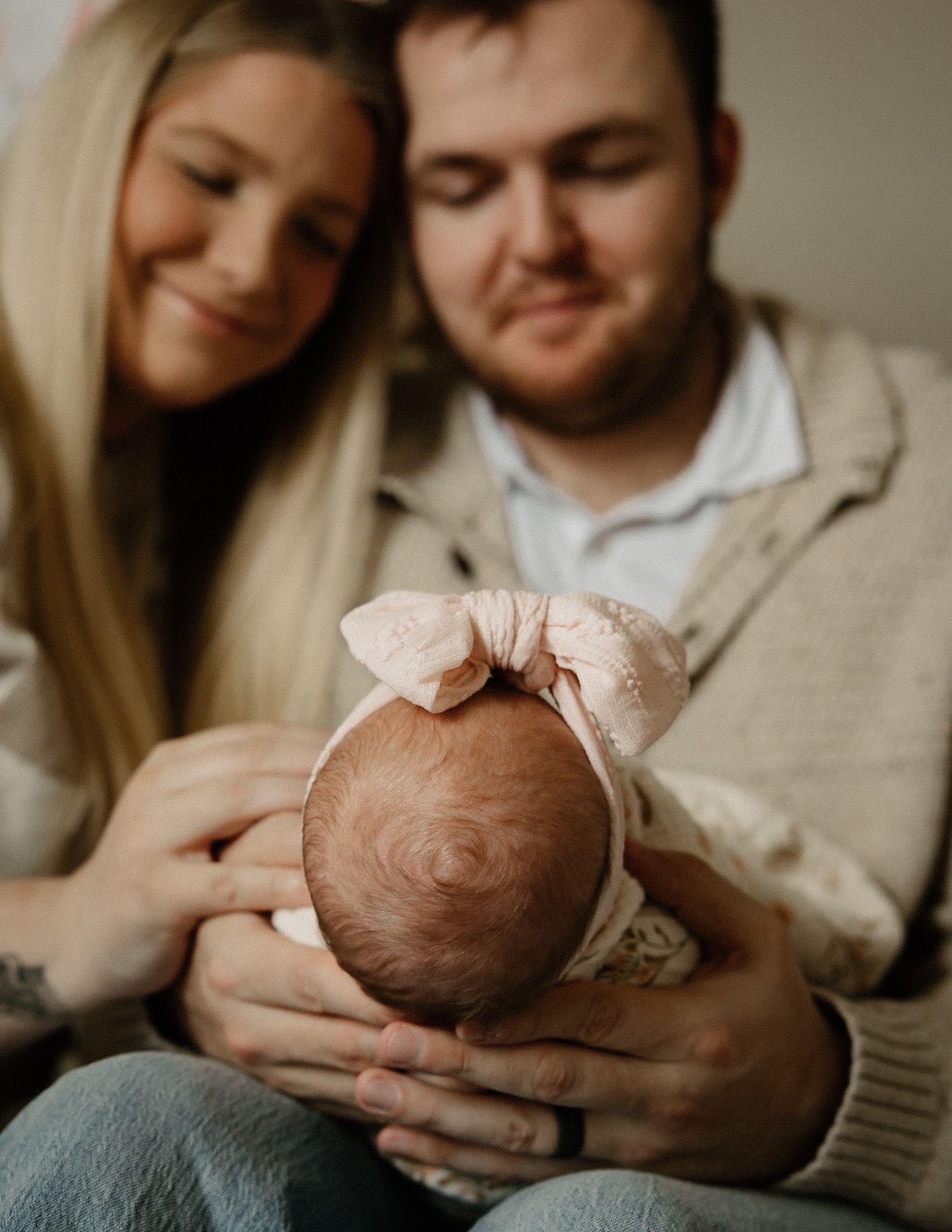 New parents lovingly gaze at their newborn baby wearing a pink bow headband.