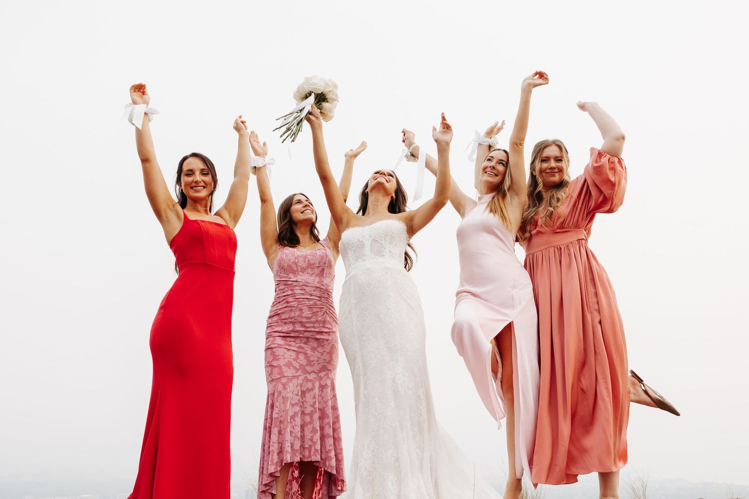 Group of women in red and pink dresses jumping and celebrating joyfully against a white background.