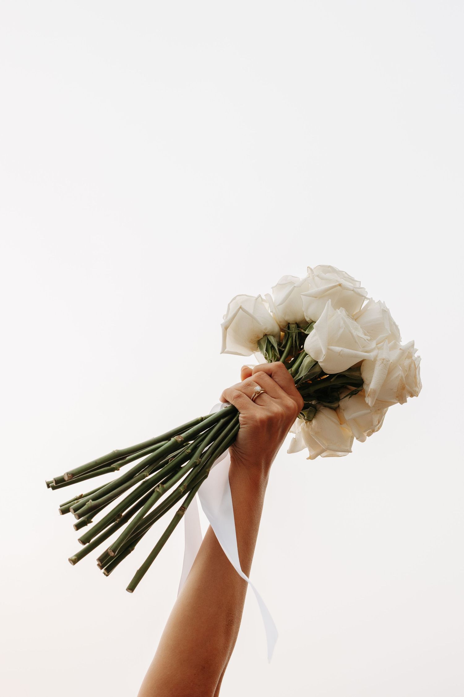 A hand holds a bouquet of white roses against a white background in a minimalist artistic composition.