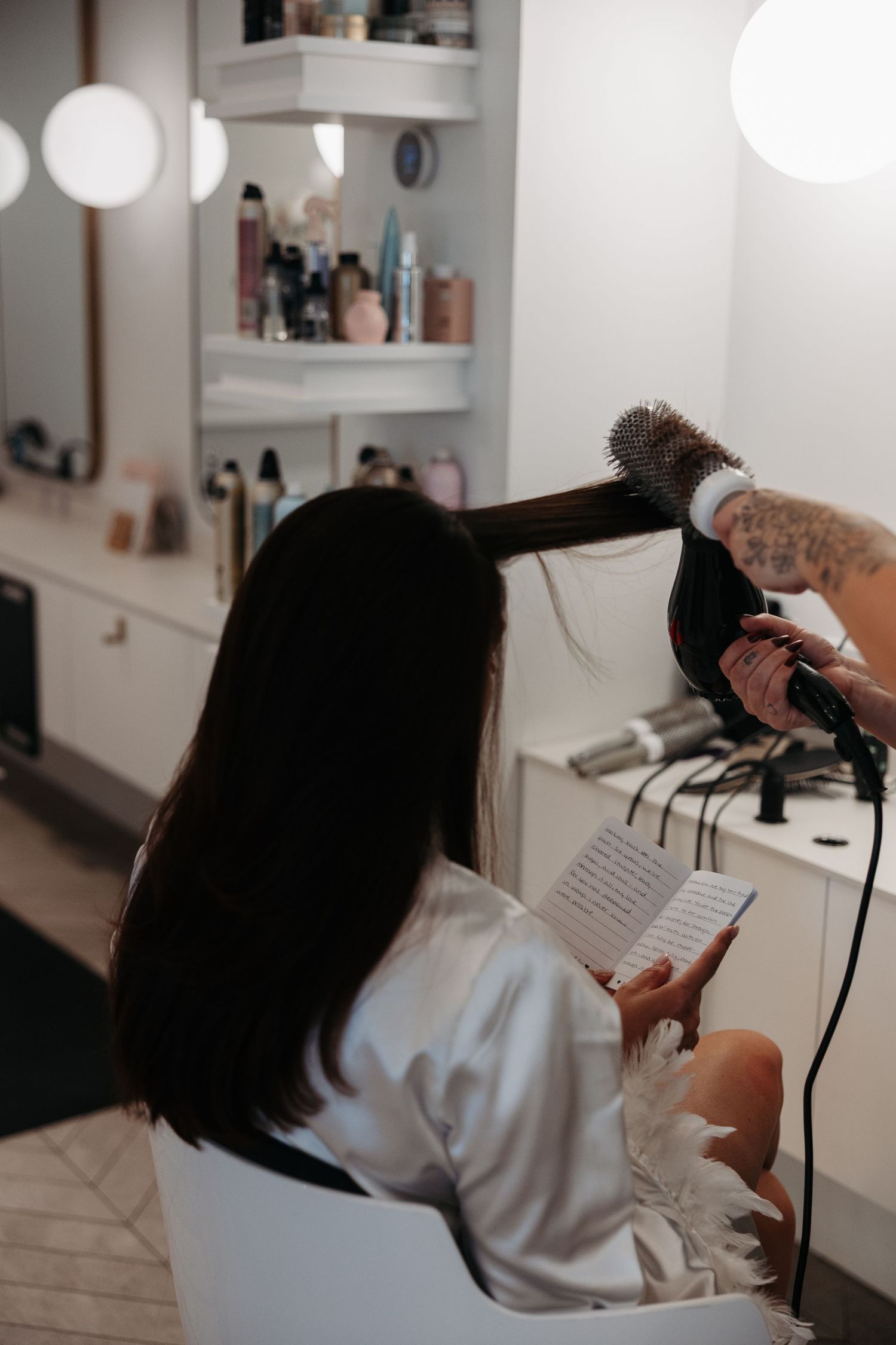 Hair stylist using professional blow dryer and round brush while styling client's hair in modern salon.