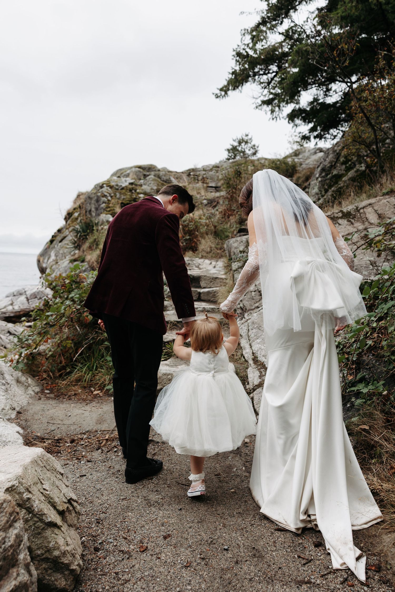 A romantic wedding couple walks along a rocky mountain trail as the bride's white veil flows in the wind.