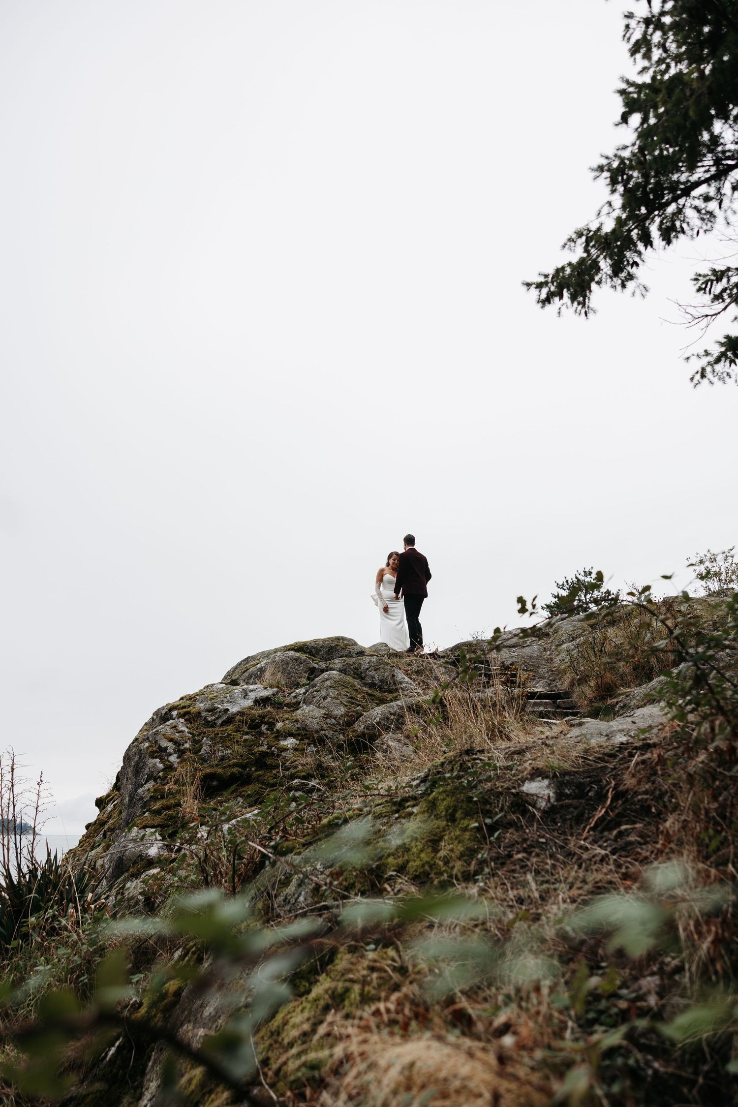 A silhouetted figure stands atop a rocky cliff edge against a misty sky during golden hour.