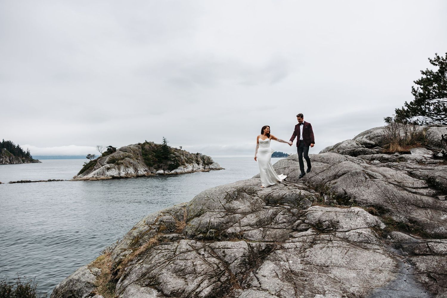 Two people stand on a rocky coastal outcrop overlooking the ocean during a cloudy day.