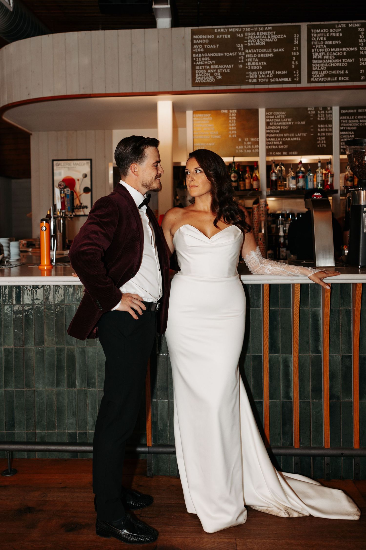 A couple shares a romantic dance sequence in formal attire at an indoor venue with a bar in the background.