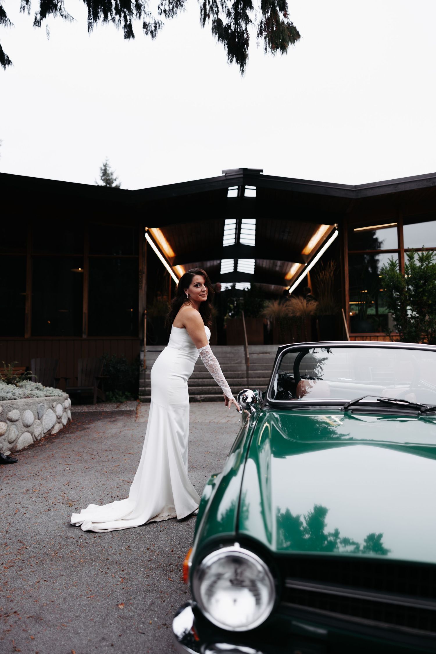 A person in a white wedding dress poses elegantly next to a classic mint green vintage car.