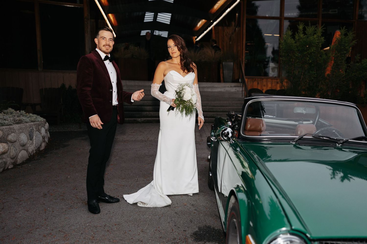 A couple in wedding attire poses next to a vintage mint green car during their wedding celebration.