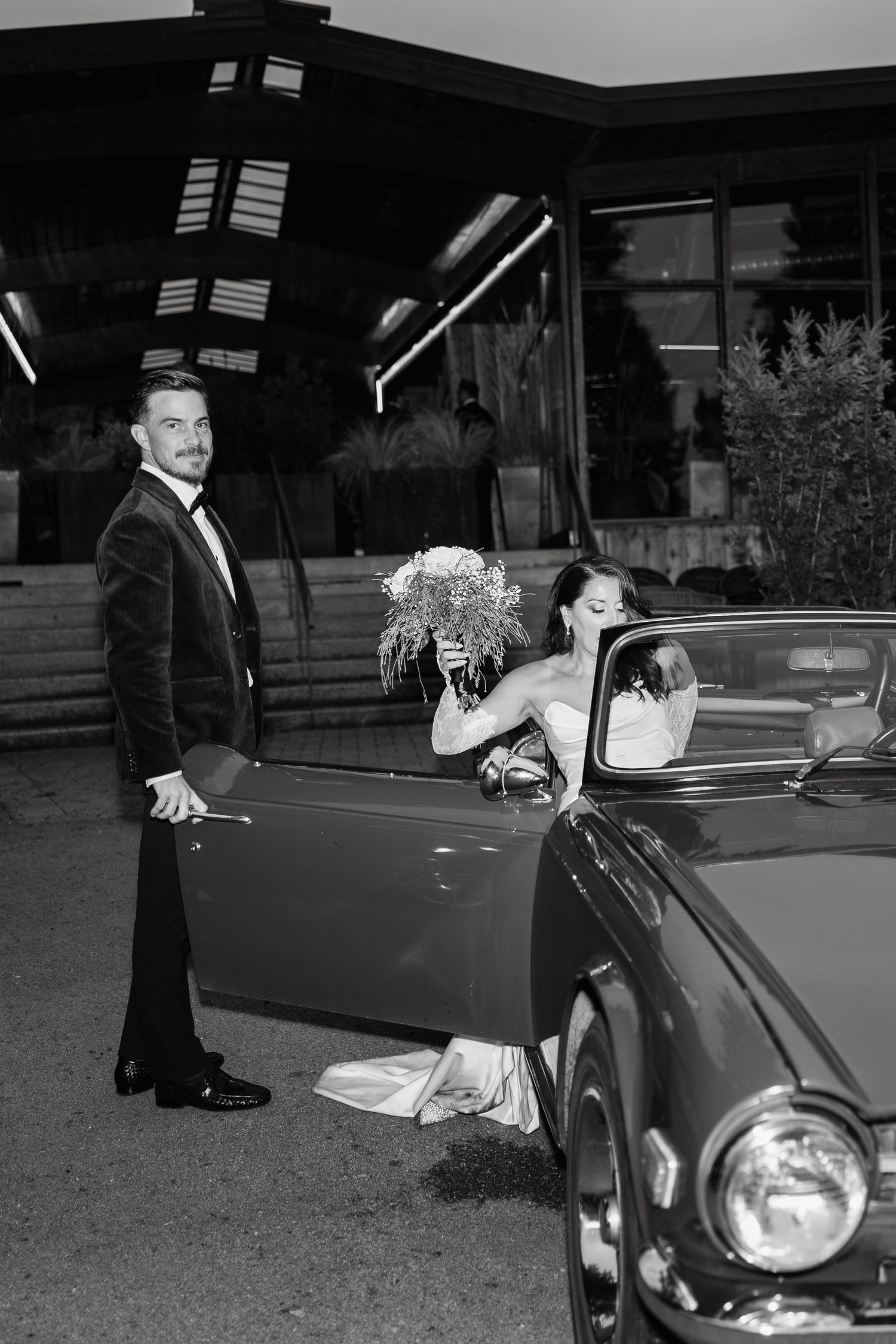A couple shares a romantic moment beside a classic car during their wedding photoshoot.