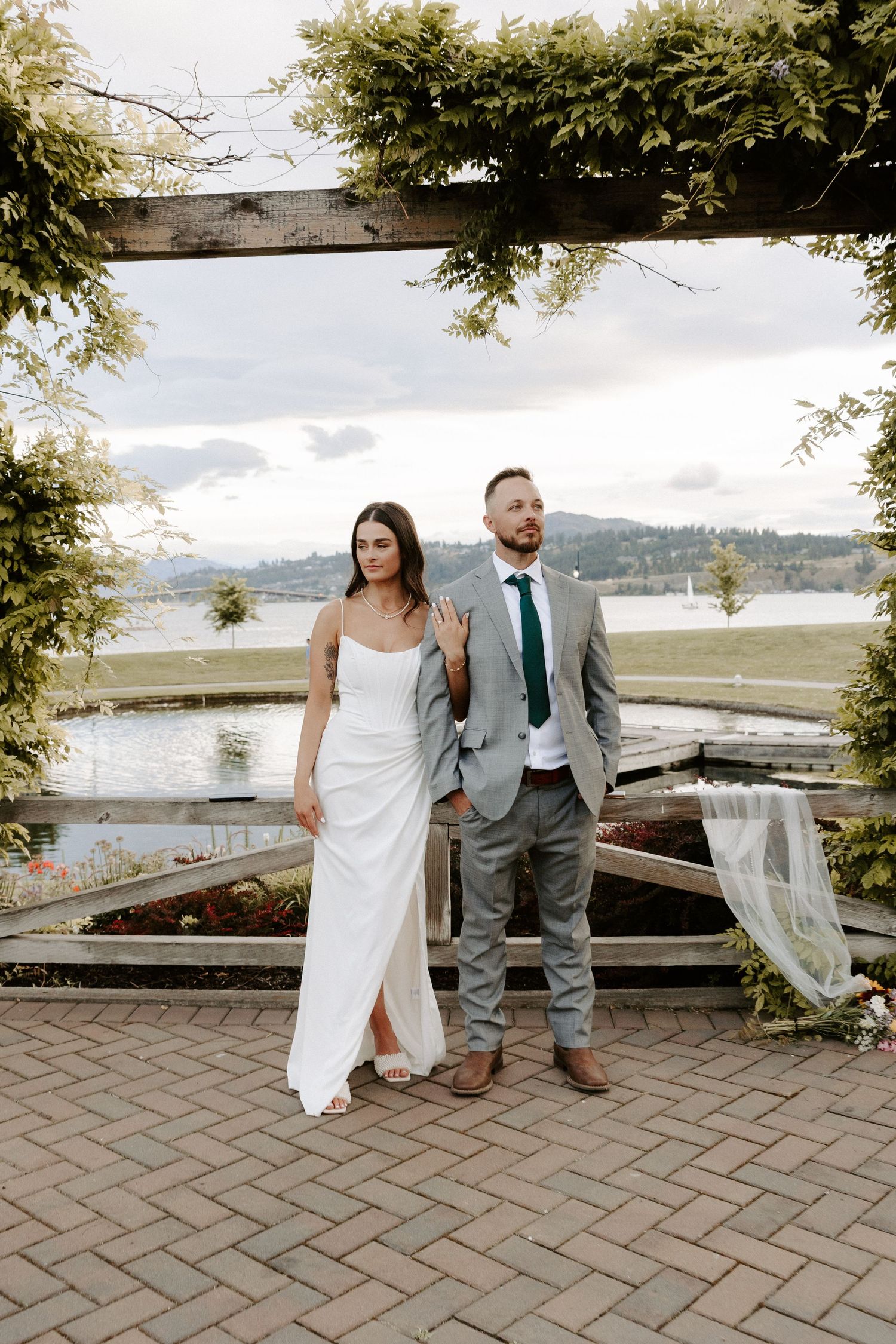 Couple in wedding attire poses for romantic photos on brick patio overlooking scenic waterfront view on their special day.