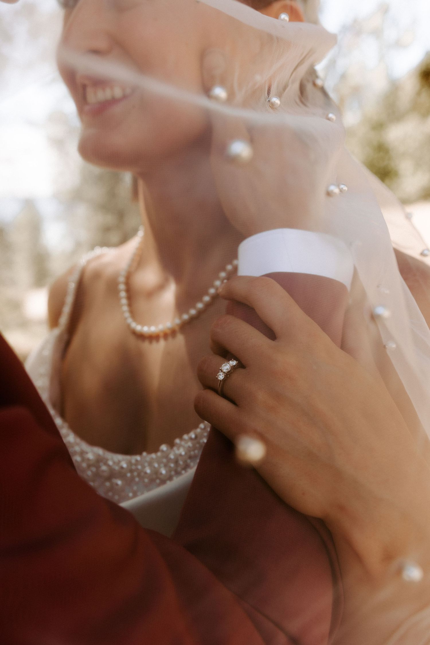 Close-up of a bride wearing a pearl necklace and beaded wedding dress, with engagement ring visible in natural light.