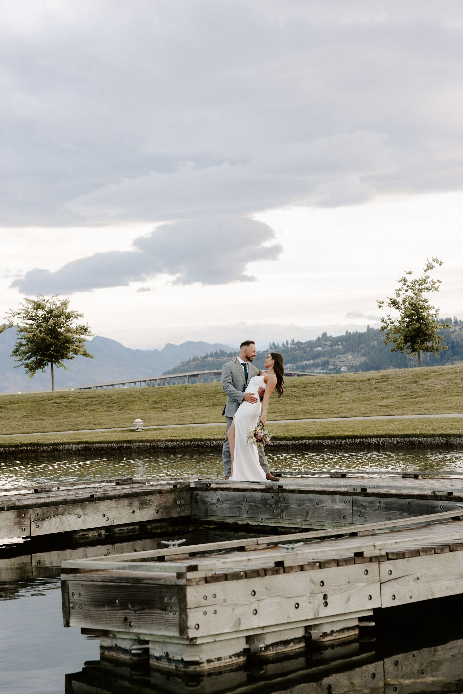 Two newlyweds share an intimate moment on a wooden dock overlooking a scenic mountain lake on their wedding day.