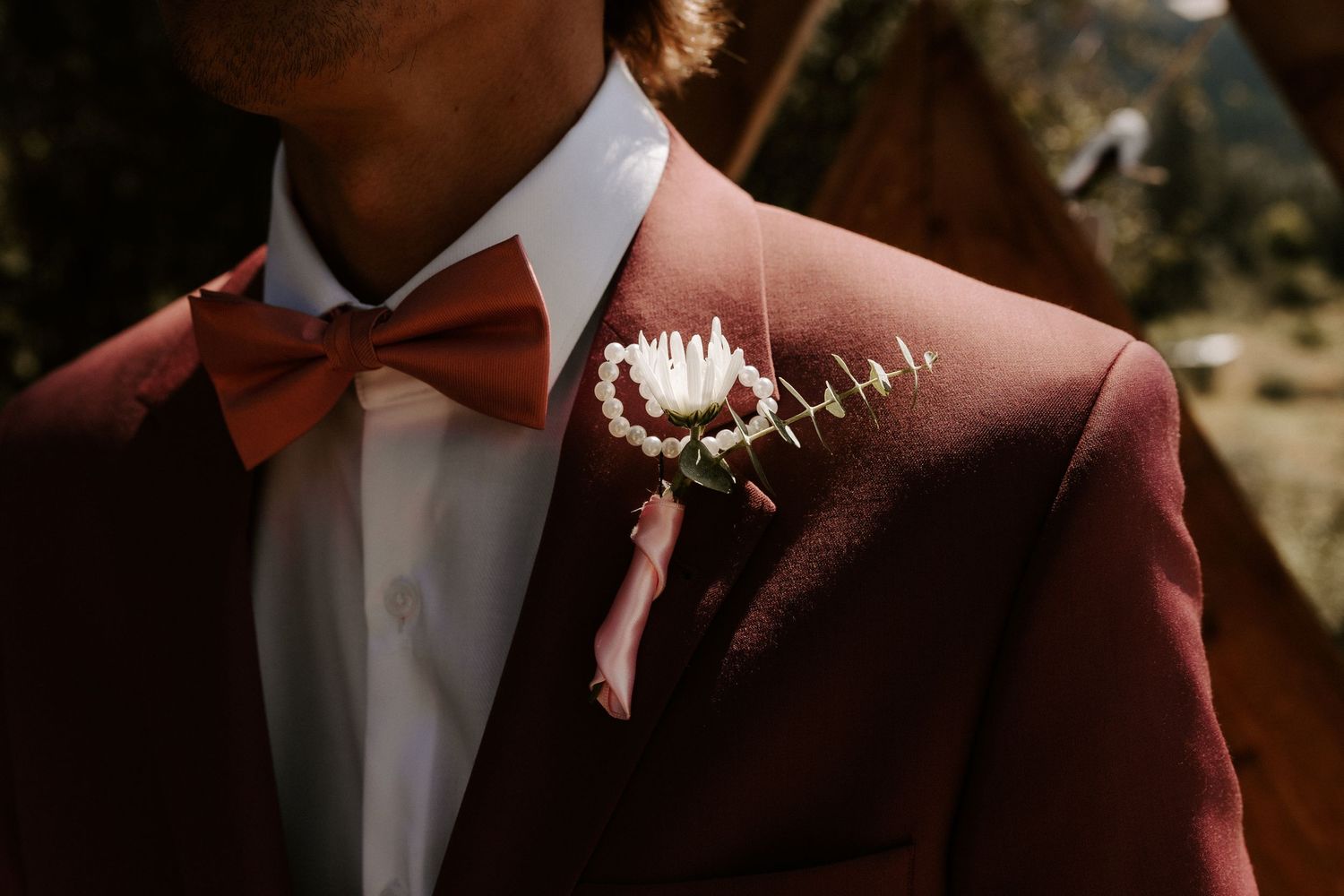 A white floral boutonniere pinned to a burgundy suit jacket with a matching bow tie.