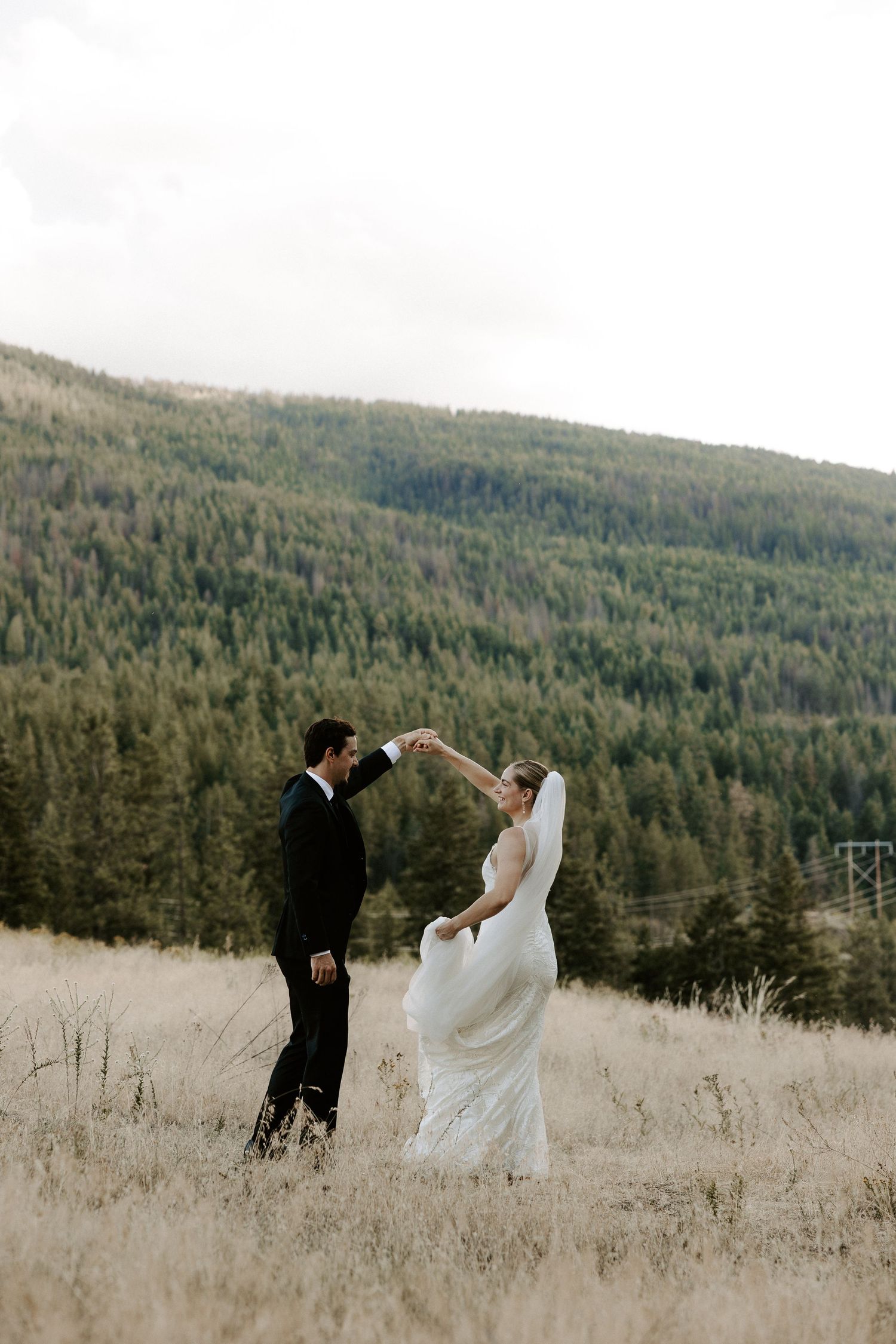 A couple sharing a romantic moment in their wedding attire against a backdrop of forested mountain slopes.