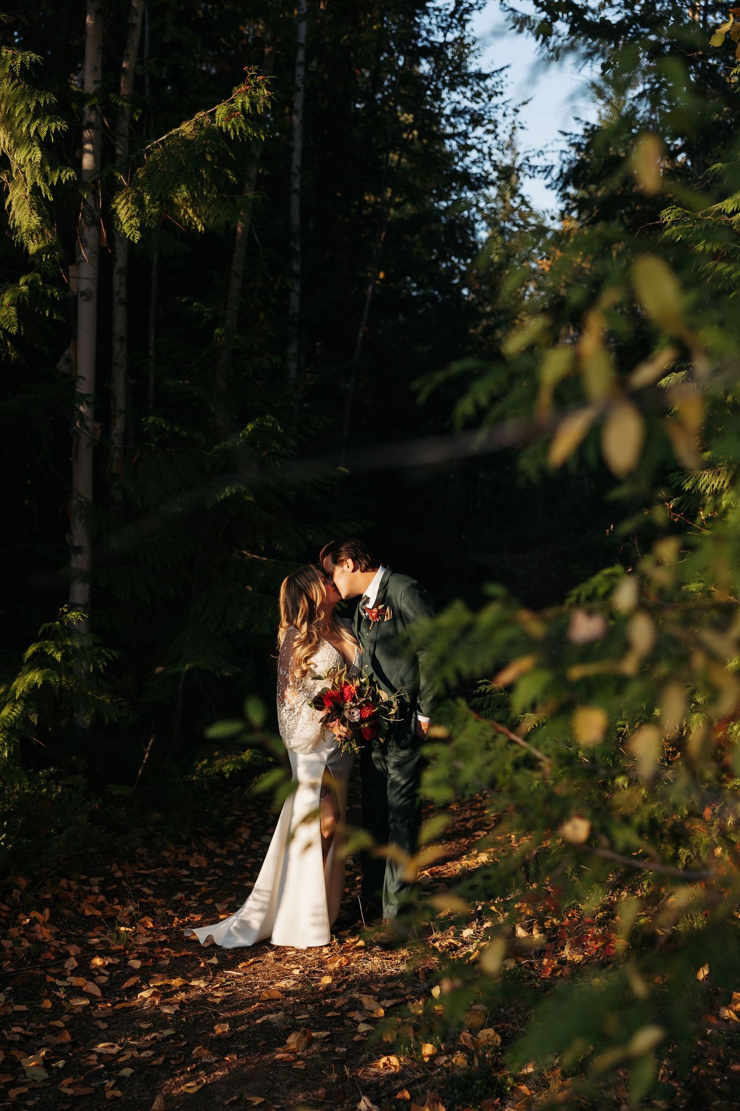 A couple embraces in a sunlit autumn forest with fallen leaves scattered on the ground.