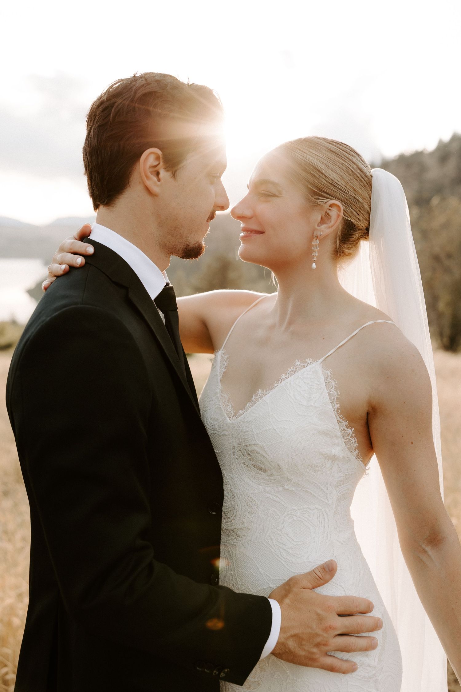 A romantic wedding photo of a couple in an intimate moment with sunlight peeking through during golden hour.