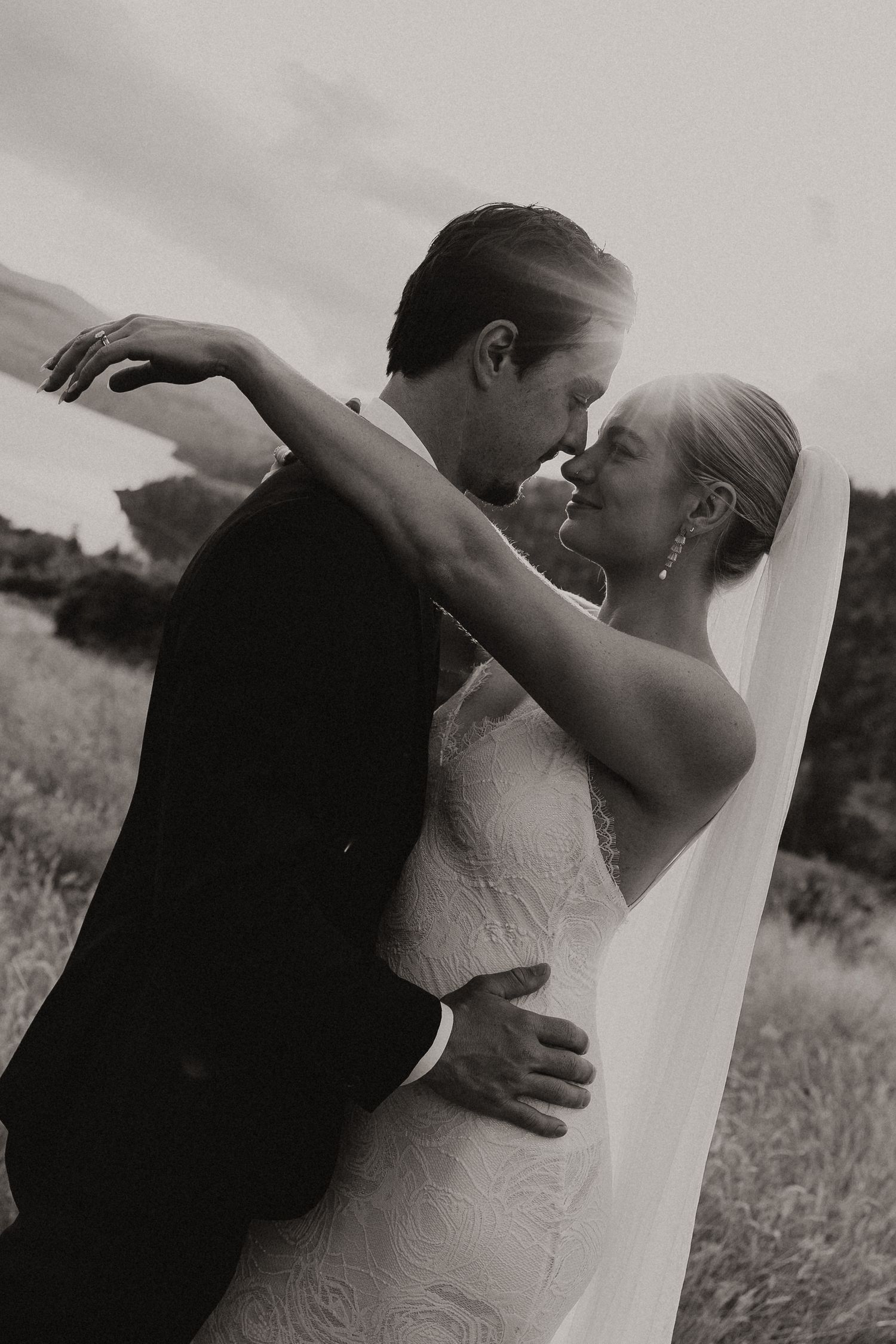 Three black and white wedding photos show a couple embracing in an outdoor field, creating a romantic sequence.