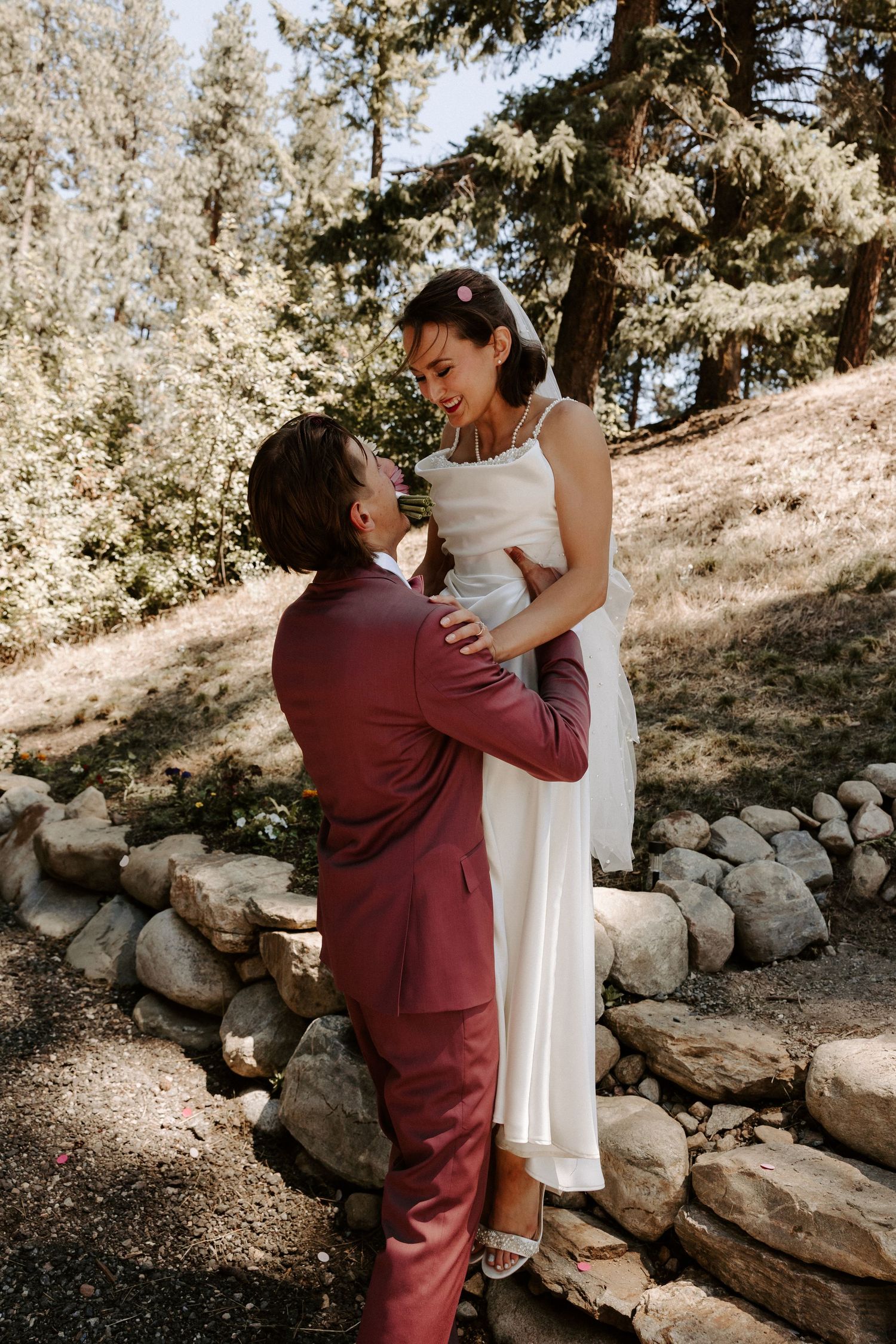 Romantic couple shares tender moment on stone steps in forest with sunlit trees in background.