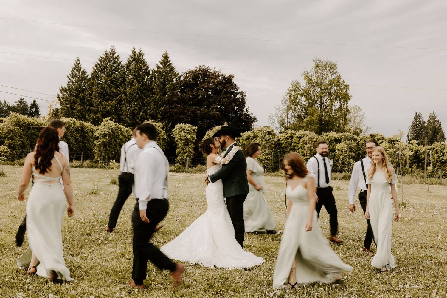 Wedding party walking together in a grassy field under cloudy skies.