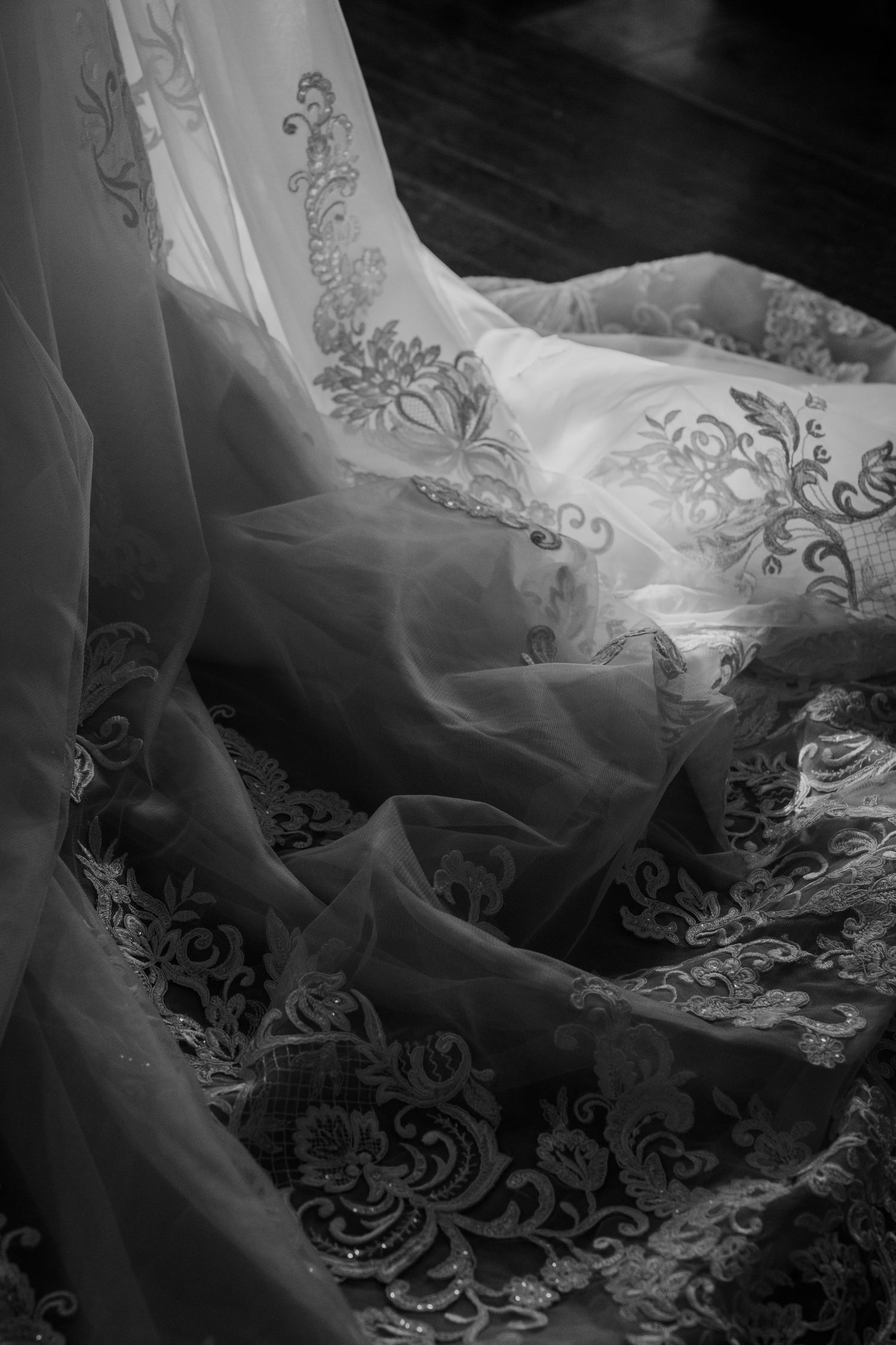 Close-up black and white detail of intricate lace patterns on wedding dress.