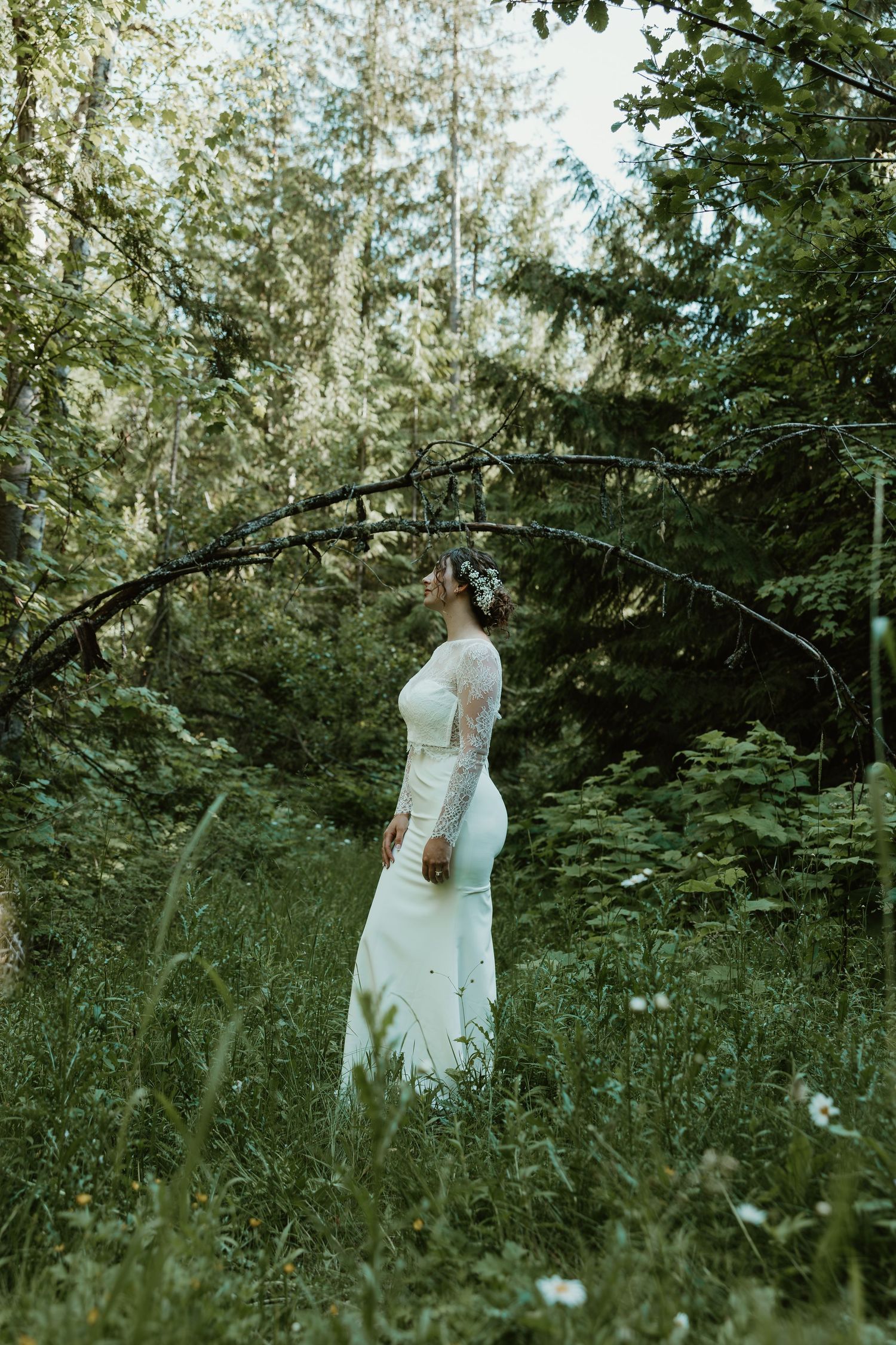 A bride in a fitted white dress poses in a mystical forest setting.