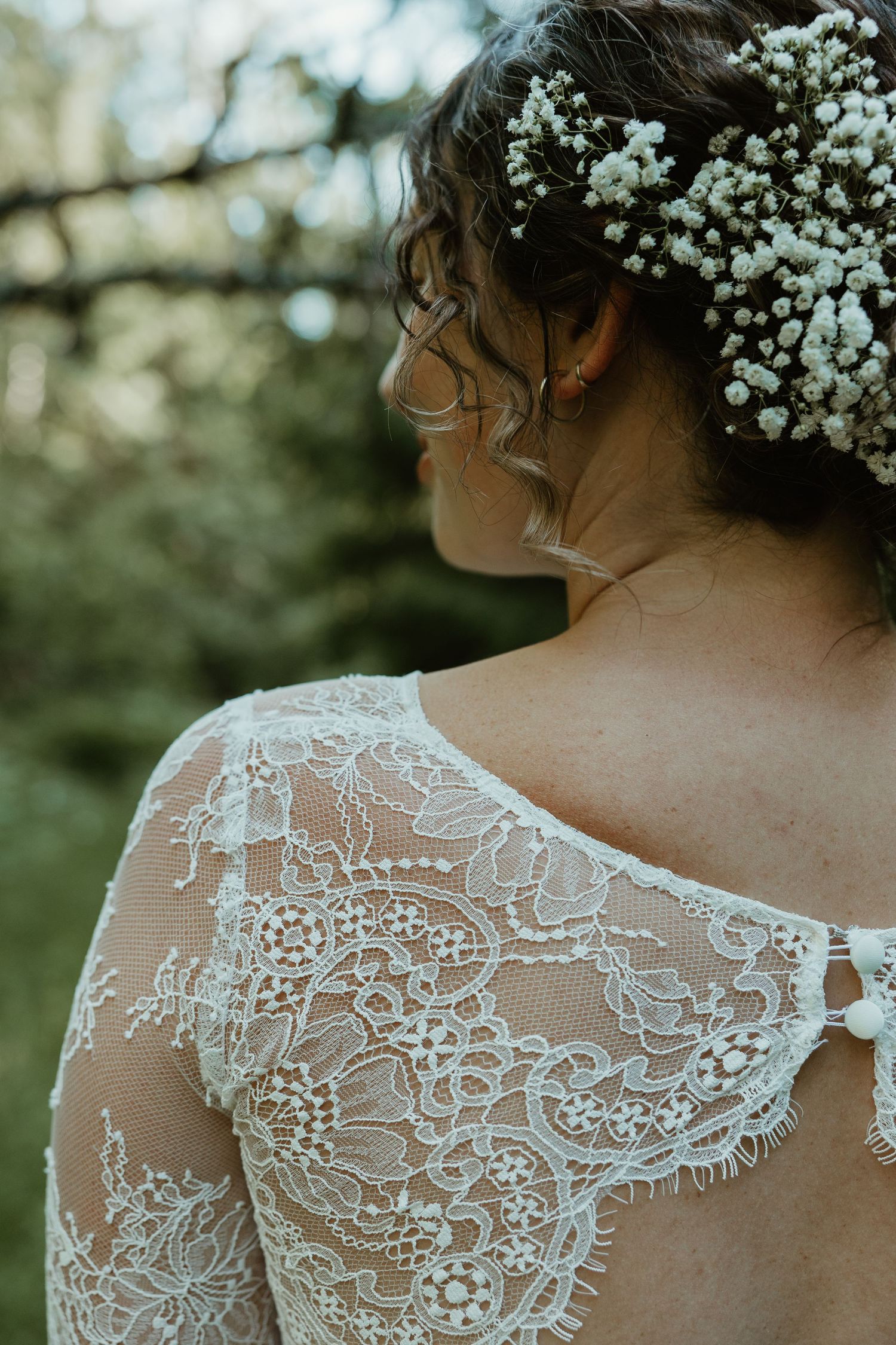 Delicate lace detail and baby's breath flowers adorn a bride's wedding dress.