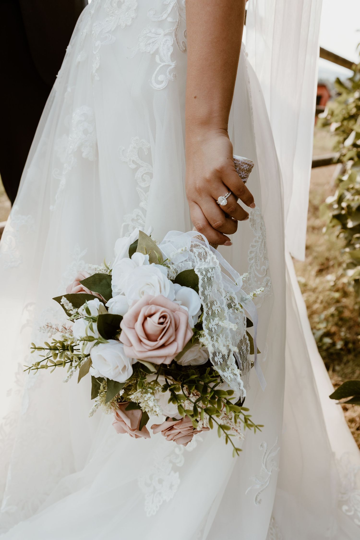 Close-up of bridal bouquet with pink roses and white flowers against lace dress.