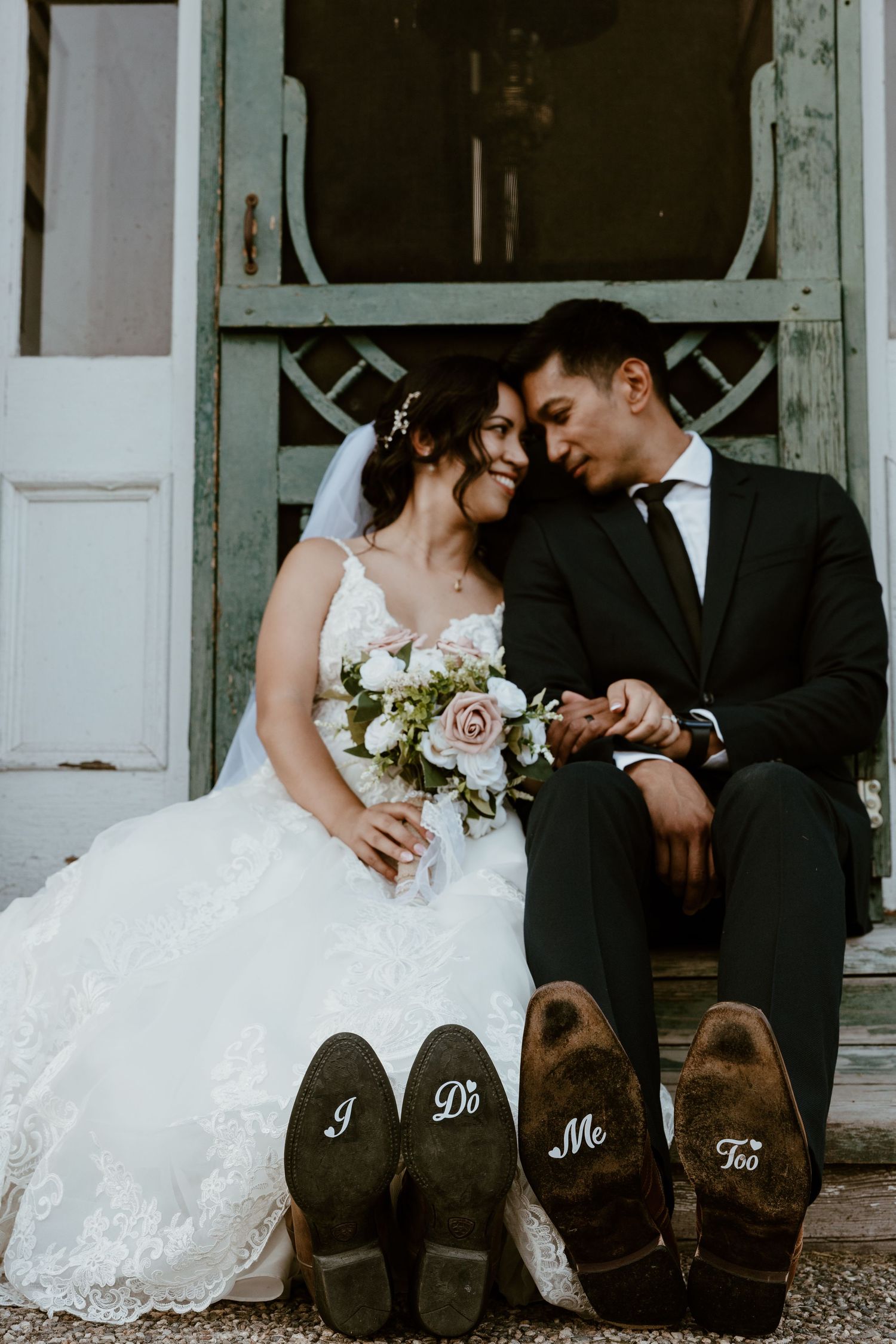 Wedding couple sits on porch steps with personalized shoes displayed below.